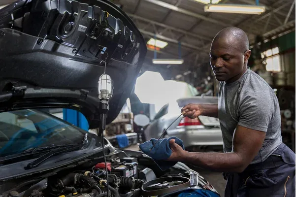 a black mechanic inspecting a car in a yard